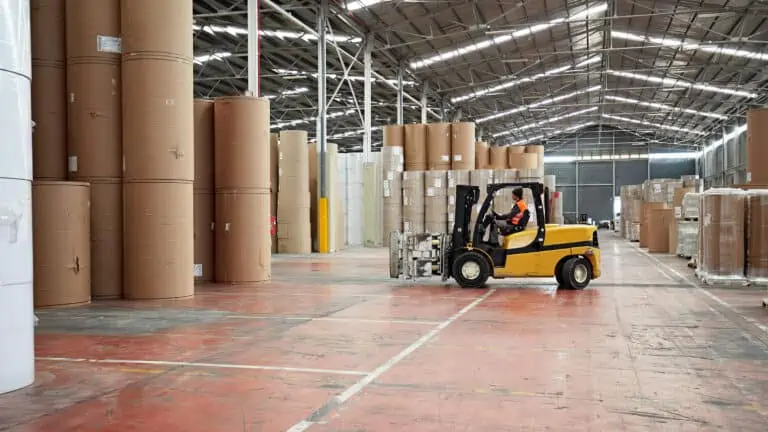 Worker driving forklift inside warehouse facility with stacked product visible