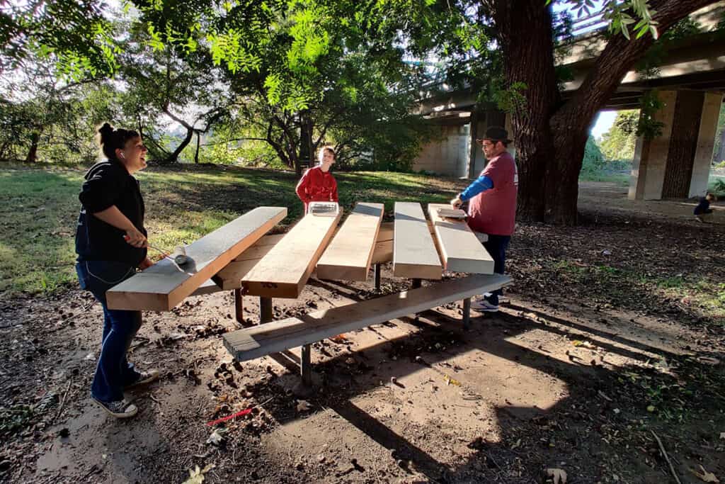 3 people staining wooden planks during an American River Parkway Foundation volunteer event