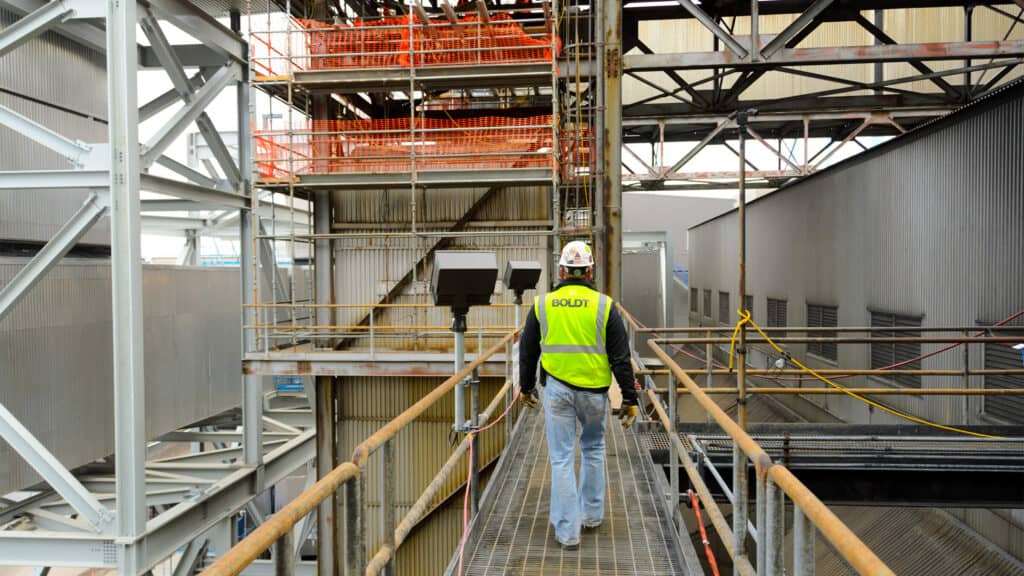 Central Utility Plant Walk - Boldt employee wearing vest walking away from camera on catwalk