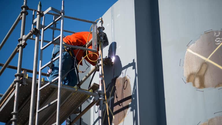 welder working on metal building from scaffold