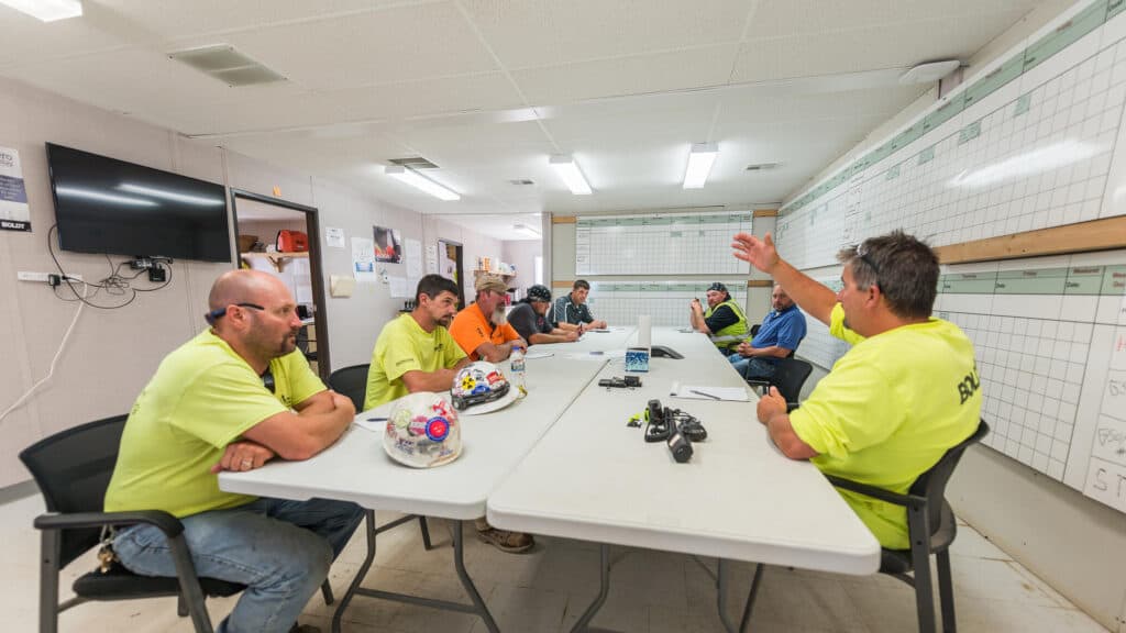 Boldt employees seated at tables in a construction trailer with the schedule and project plan visible on the walls behind them