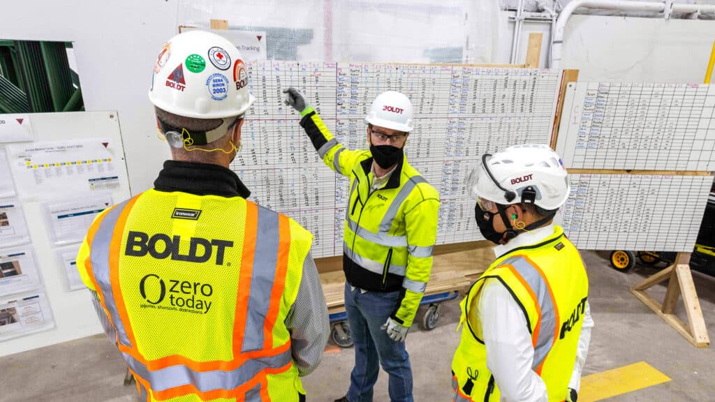 Lean Construction Services. 3 Boldt employees standing around whiteboards of data