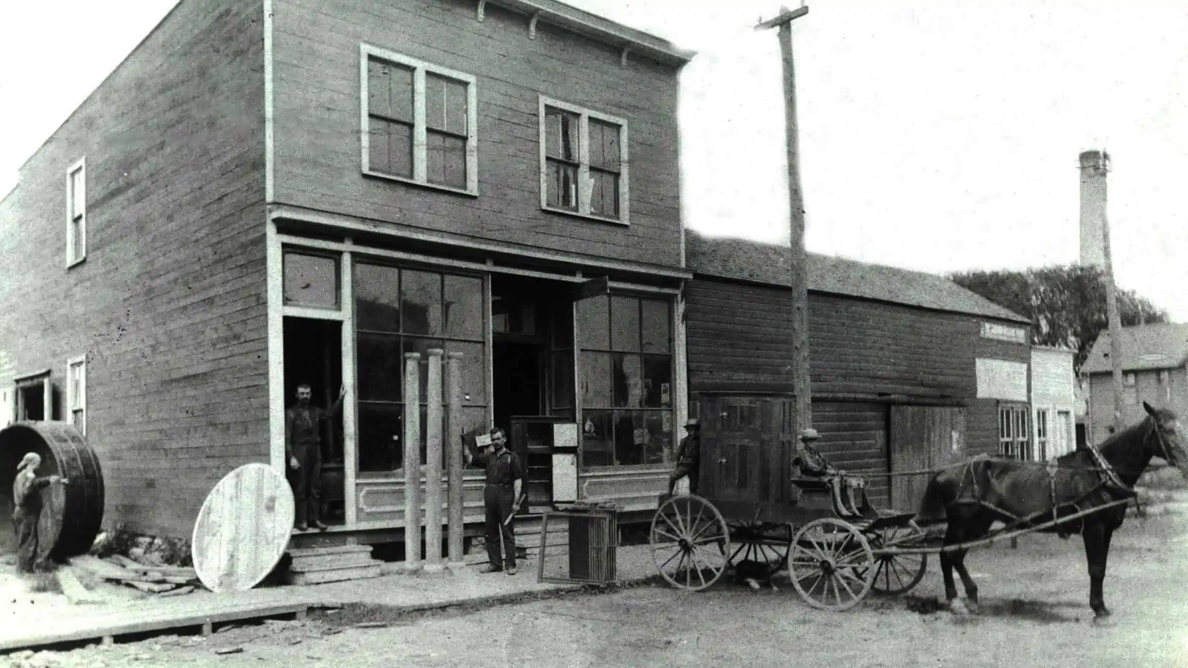 Black and white photo of horse-drawn carriage in front of woodworking shop