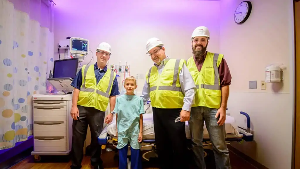 Construction workers posing for photo with little boy in hospital room