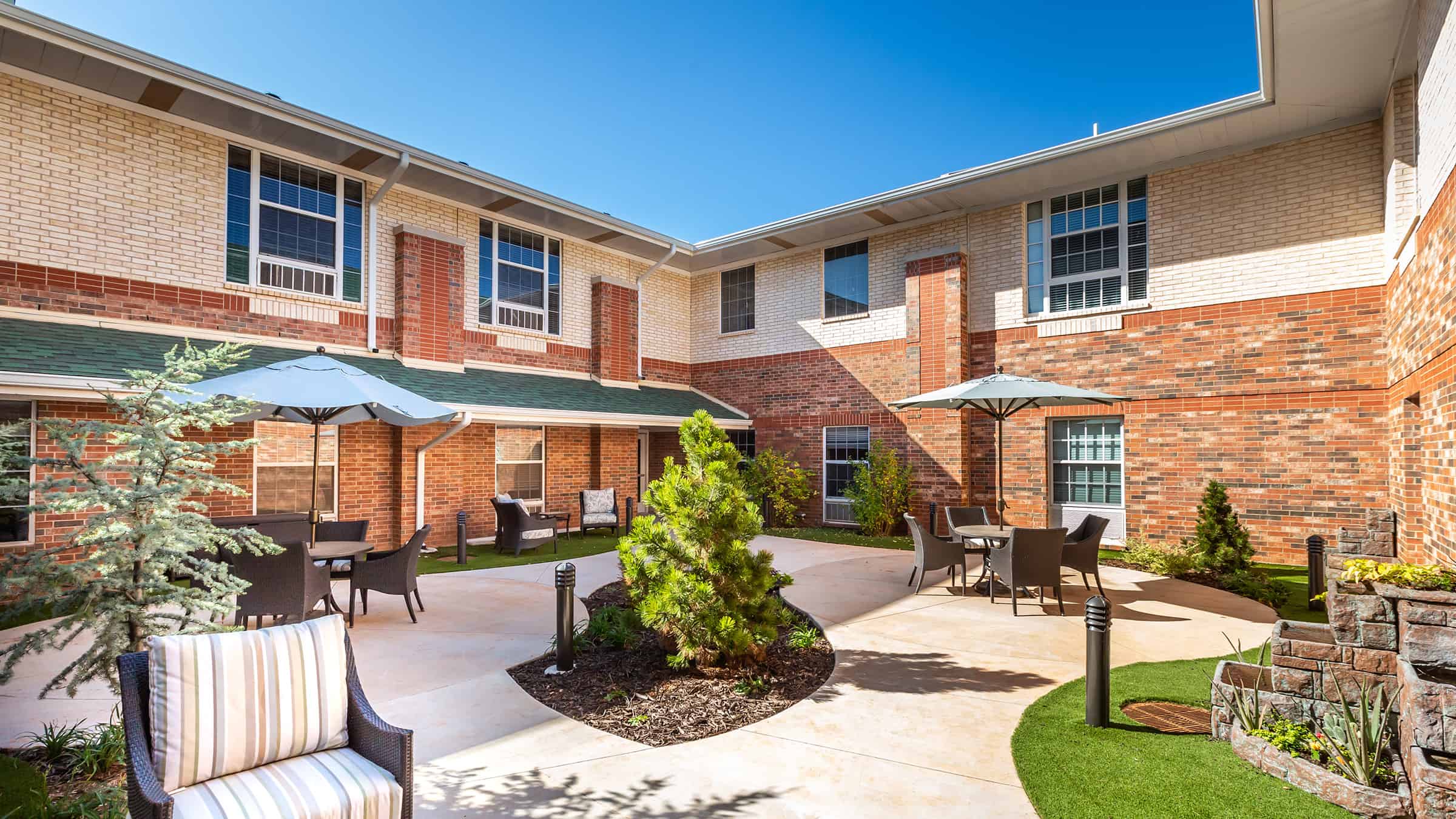 Spanish Cove Retirement Community Exterior of Building with Courtyard Seating, Umbrella-covered Tables